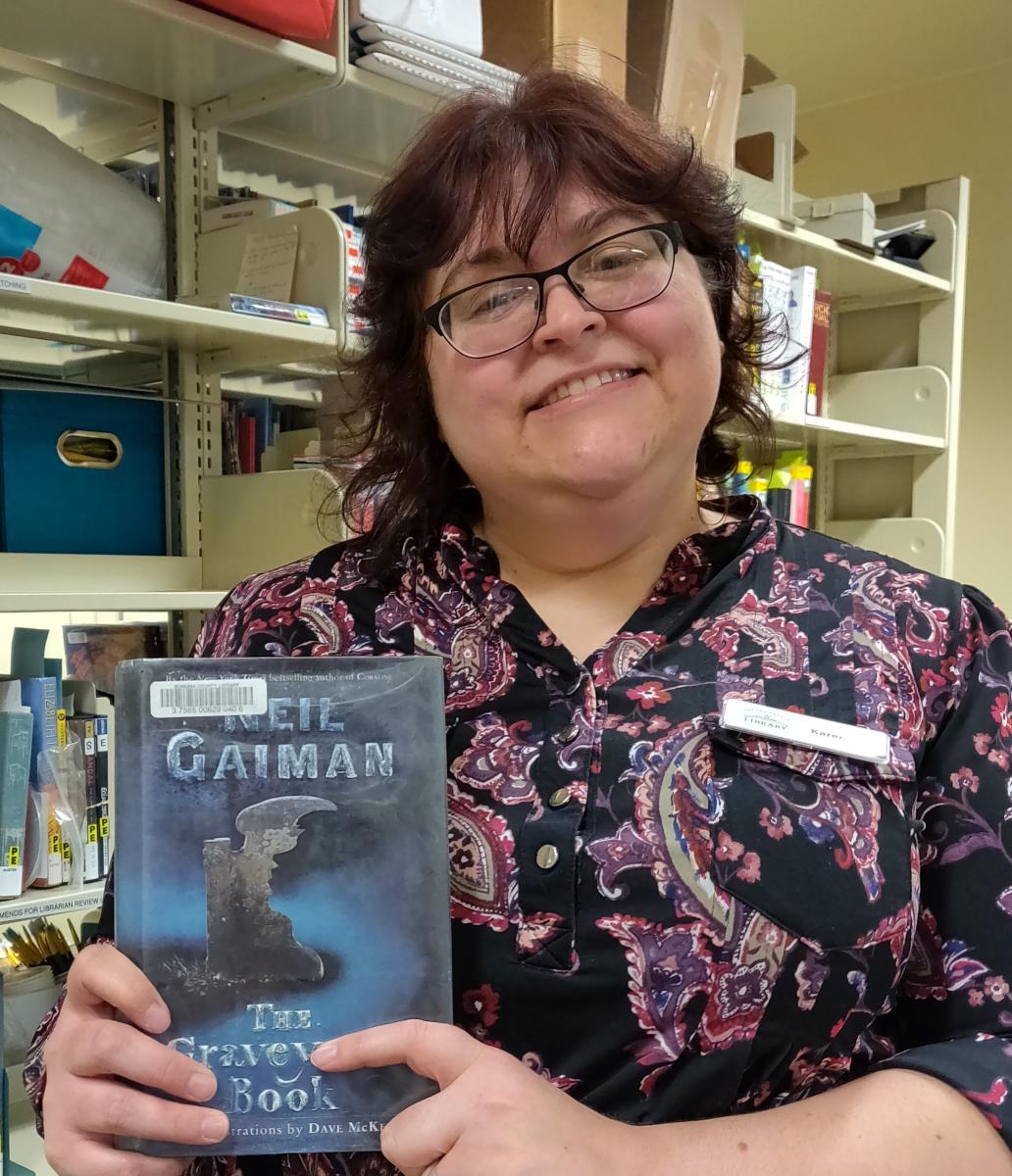 woman holding book "The Graveyard Book" by Neil Gaiman