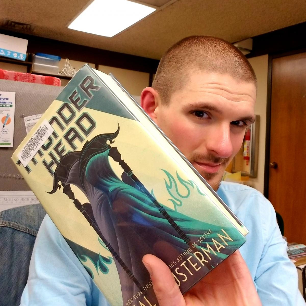 man holding book "Thunderhead" by Neal Shusterman